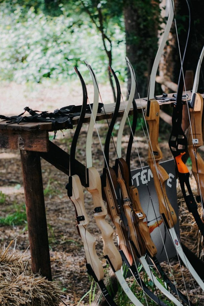 Vertical shot of various bows displayed outside on a wooden rack, surrounded by nature.